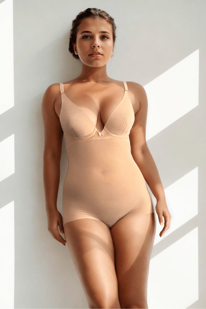 Woman wearing a beige Ender Legard bodysuit shaper with briefs standing against a white background