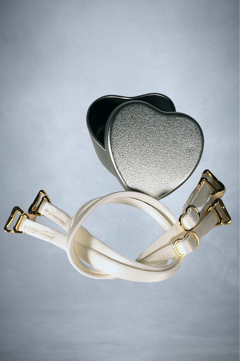 Close up view of a pair of spaghetti bra straps in colour ivory with silver presentation tin. 