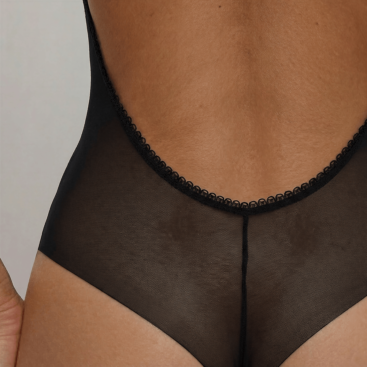 Close-up of the LEXI Black backless bodysuit's low back, showing the trimmed edge and fine power-mesh weave above the tanga's centre-back seam.