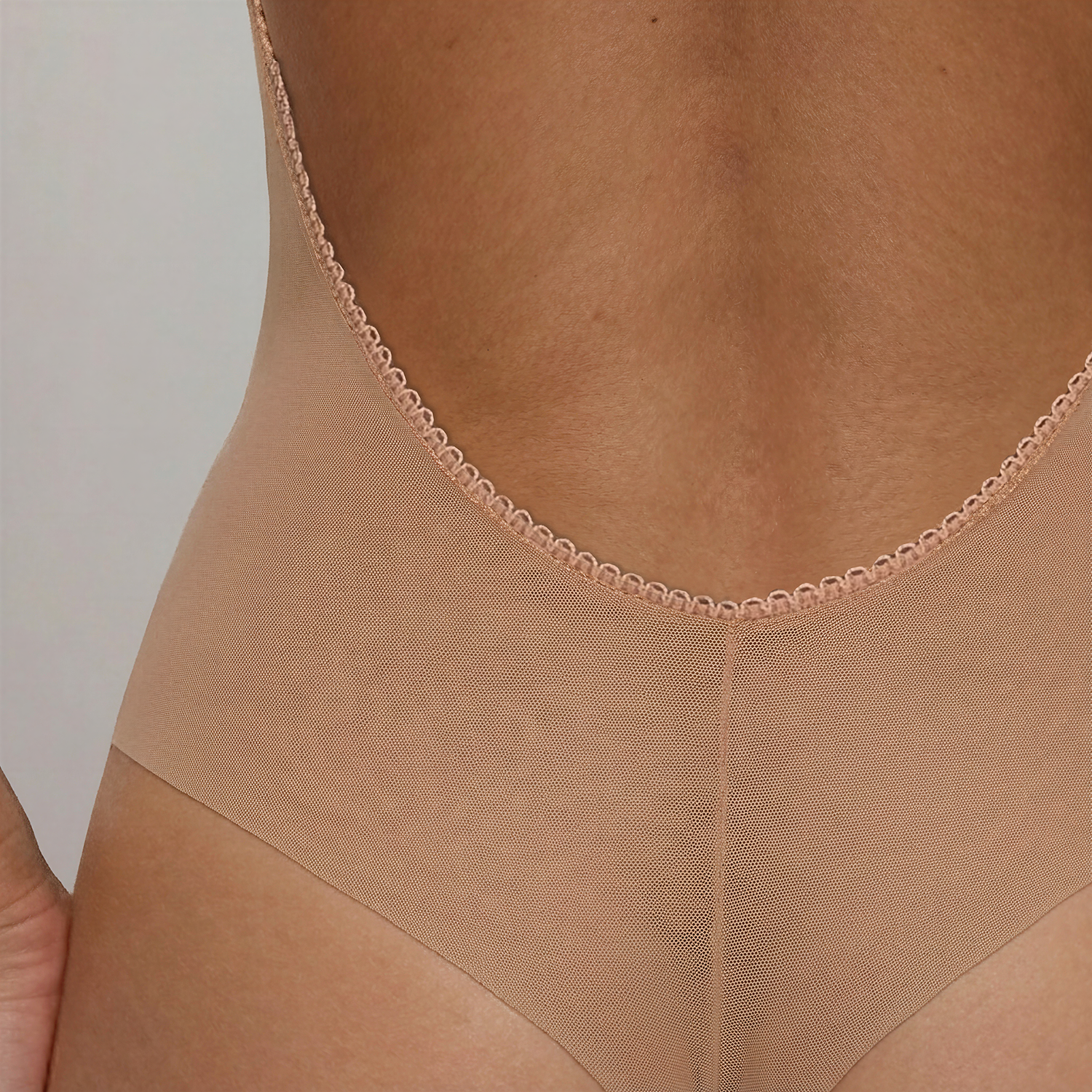 Close-up of LEXI Nude showing the low-back edge, fine power-mesh texture and centre-back seam above the high-leg tanga.