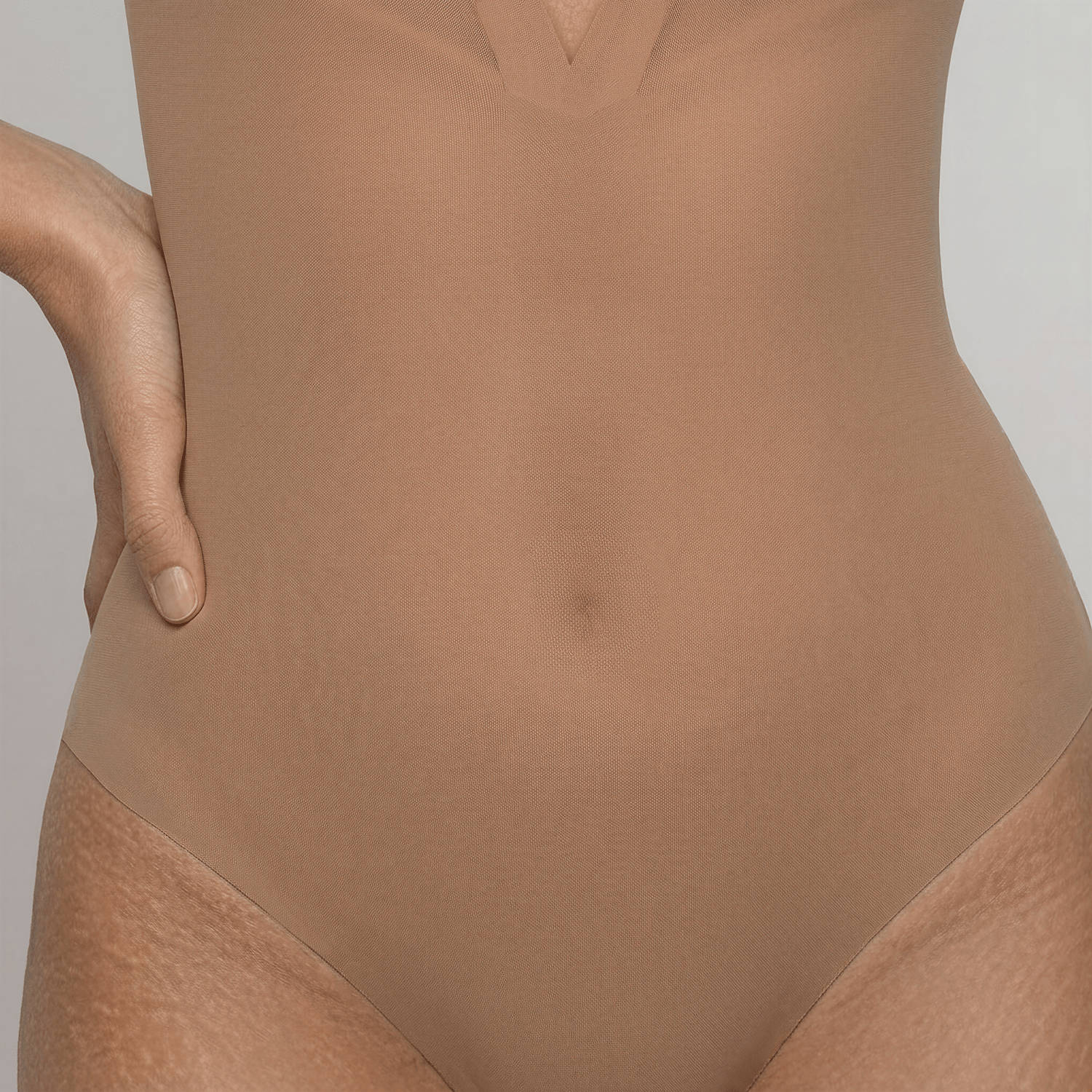 Close-up of the LIV Nude bodysuit's smooth power-mesh front, softening the belly-button's outline down to the high-leg tanga edge.