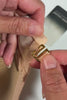 Close up on hands demonstrating how to fasten an Ender Legard Nude cross-over strap to a gold-toned G-hook to secure the strap to the bodysuit.